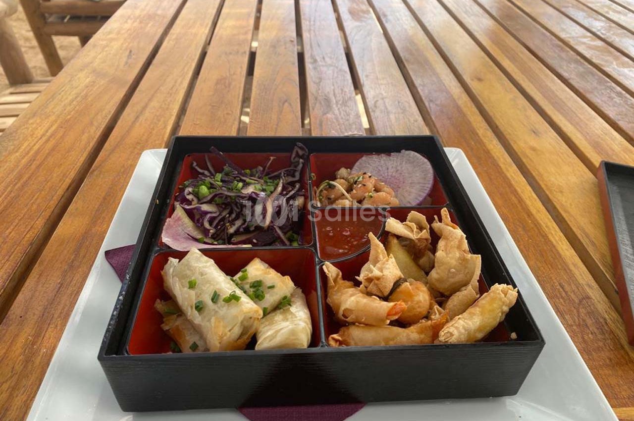Plateau compartimenté contenant des rouleaux de printemps, crevettes frites, salade de chou rouge et sauce.