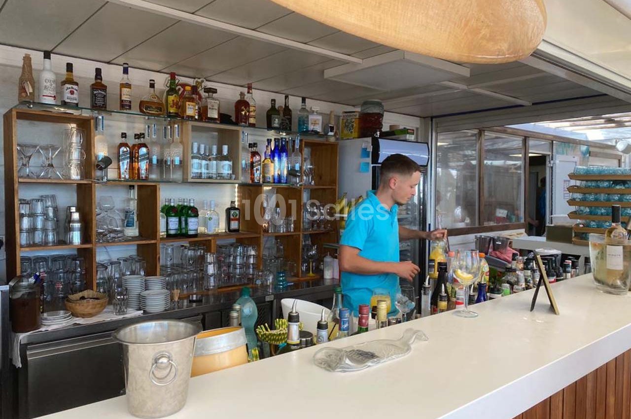 Un barman prépare des boissons derrière un comptoir blanc dans un bar bien approvisionné.