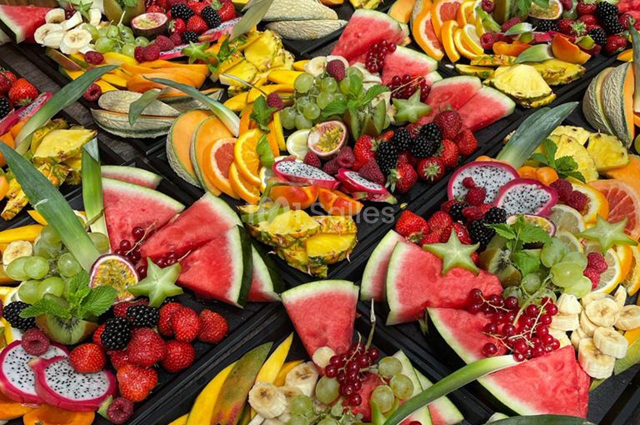 Plateaux garnis de fruits variés tels que pastèques, ananas, raisins, fraises, fruits du dragon et tranches d'agrumes.