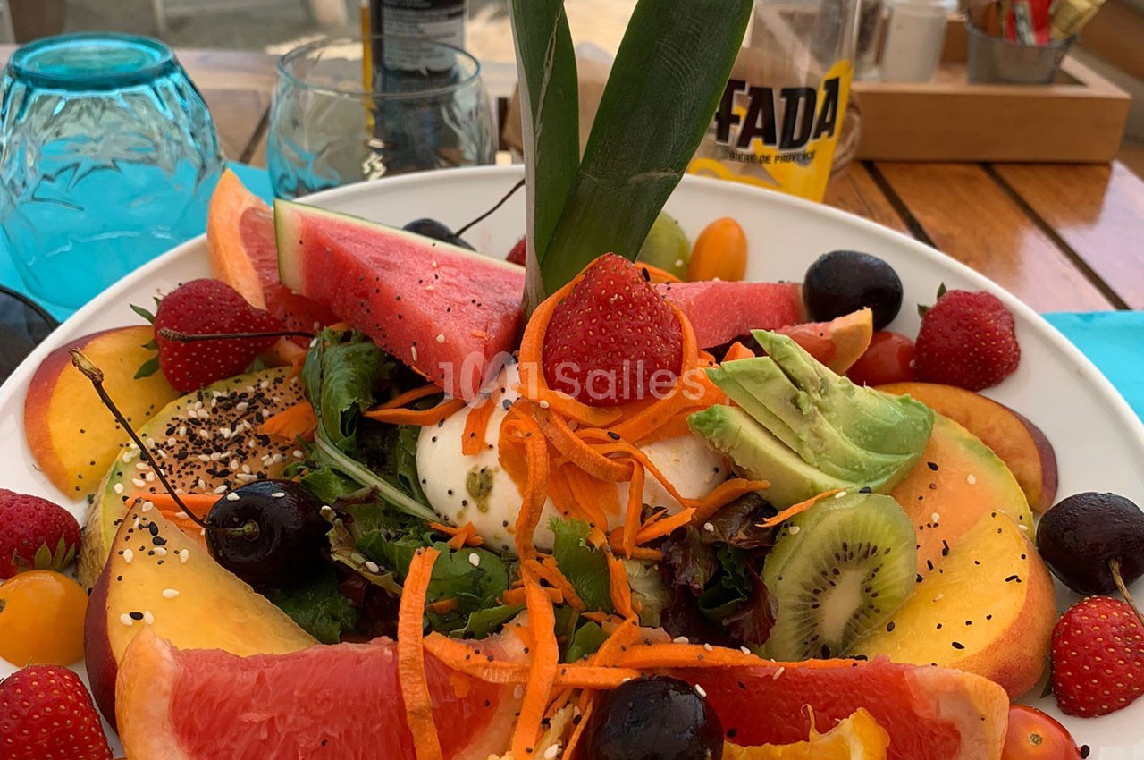 Assiette colorée de fruits frais variés, légumes, avocat et burrata, servie sur une table en bois.