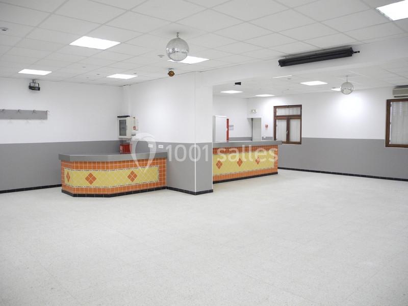 Salle vide avec comptoir carrelé jaune et orange, murs blancs et gris, sol clair et plafond avec éclairage intégré.