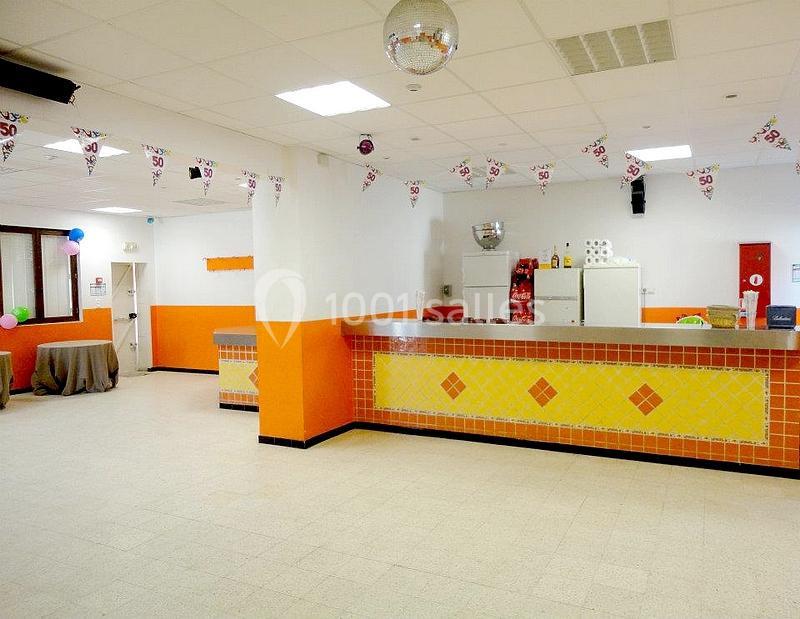Salle lumineuse avec comptoir carrelé jaune et orange, décorée de guirlandes festives et équipée d'un réfrigérateur.