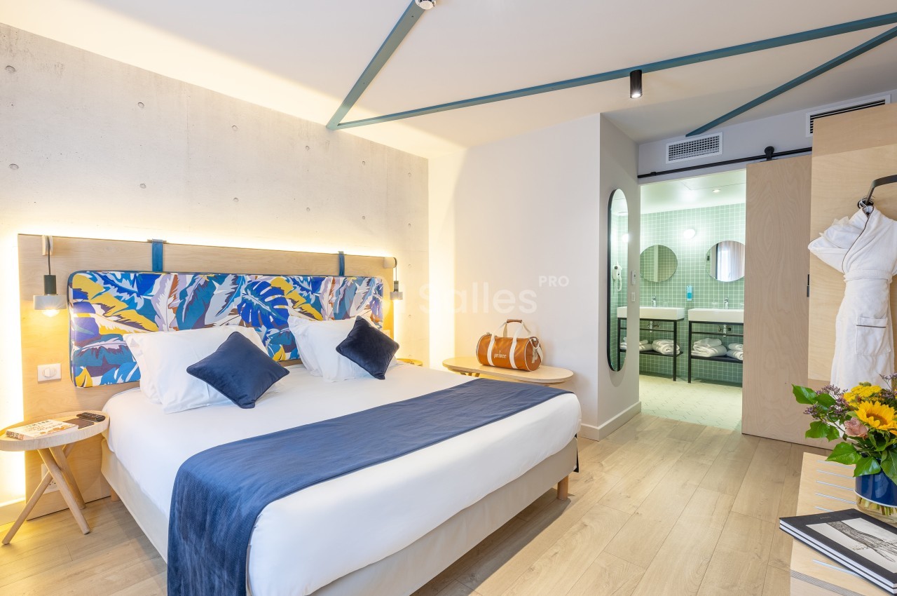 Chambre lumineuse avec lit double, décoration colorée, salle de bain attenante et détails modernes.
