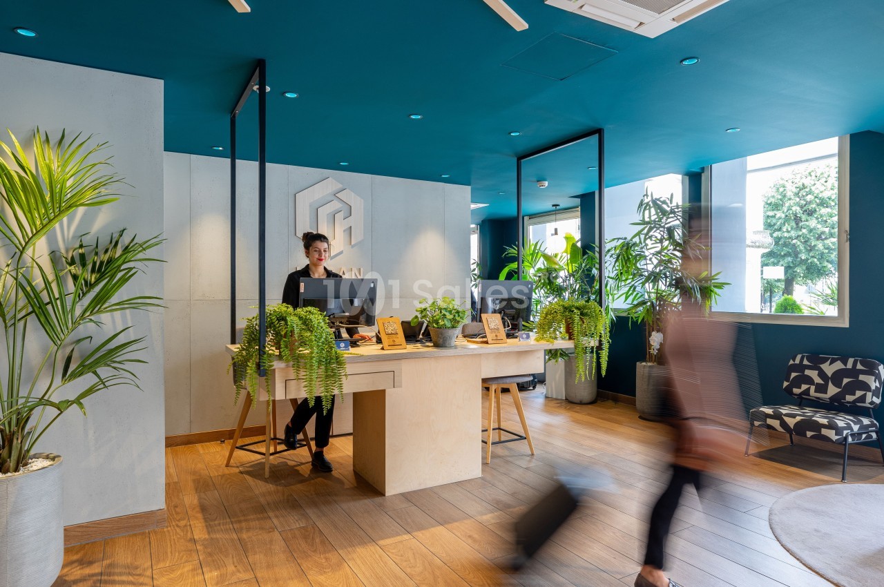 Accueil moderne avec comptoir en bois, plantes décoratives et une personne souriante dans un espace lumineux.
