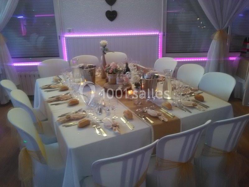 Table élégamment dressée pour un repas, avec nappes blanches, couverts, verres, pains et décorations florales.