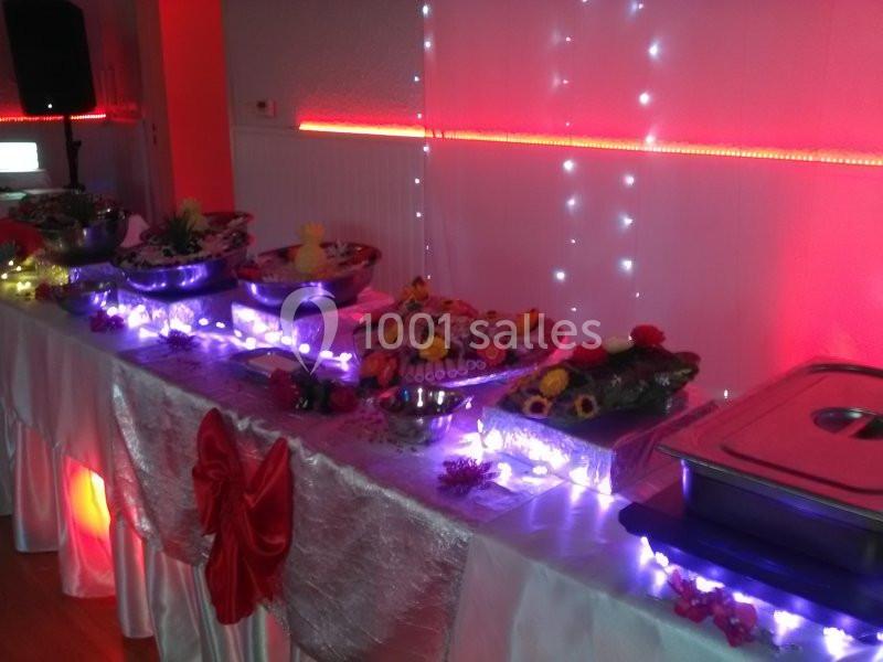 Buffet décoré avec des fleurs et des guirlandes lumineuses, installé sur une table drapée dans une ambiance rouge et festive.