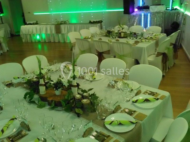 Salle de réception décorée avec des tables dressées, nappes blanches, centres de table végétaux et éclairage vert.