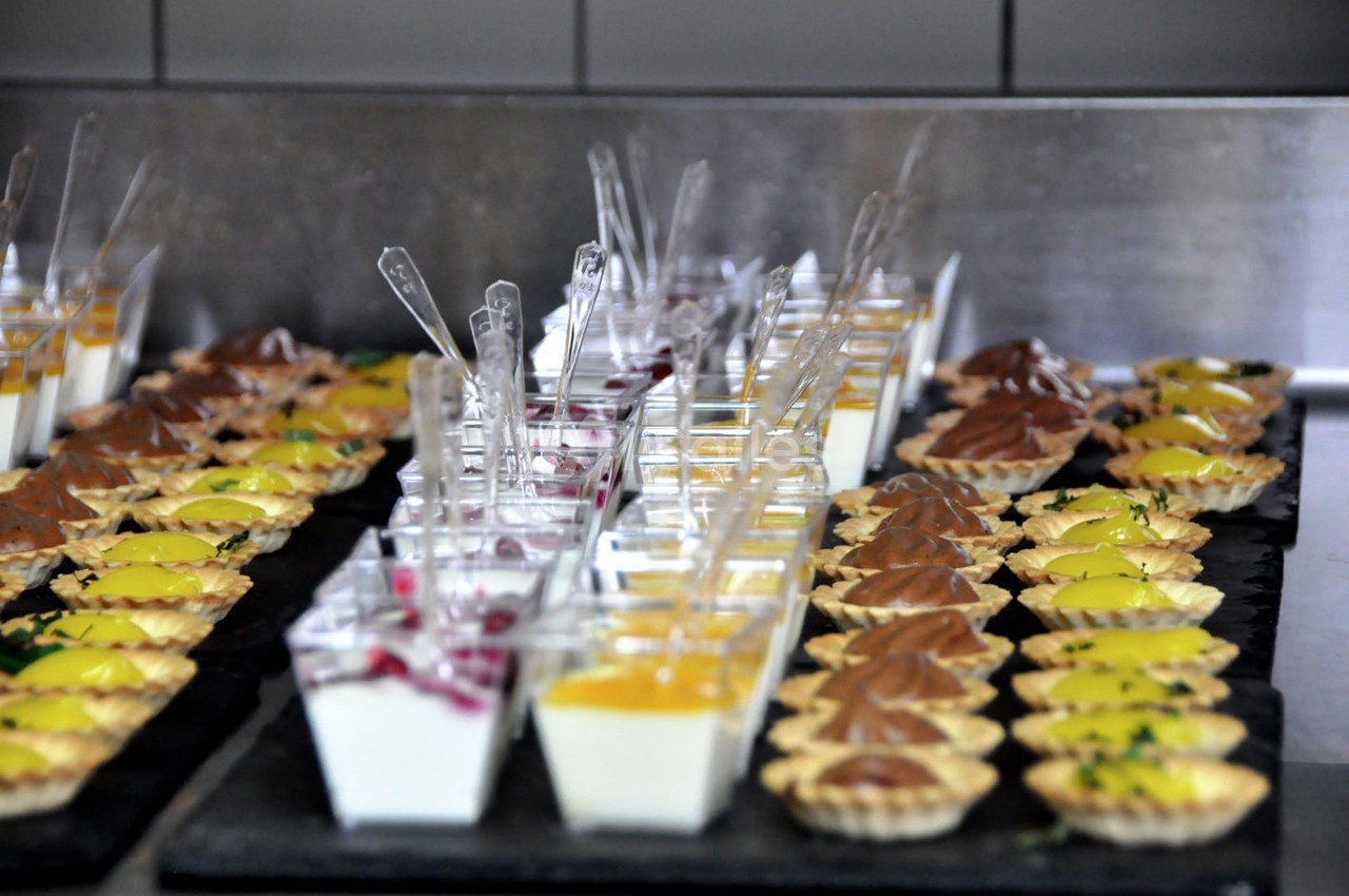 Assortiment de verrines et tartelettes sucrées disposées sur un plateau dans une cuisine professionnelle.