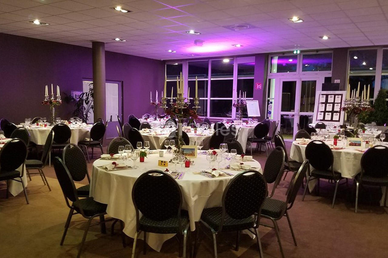 Salle de réception avec tables rondes dressées, chandeliers et éclairage d'ambiance violet.