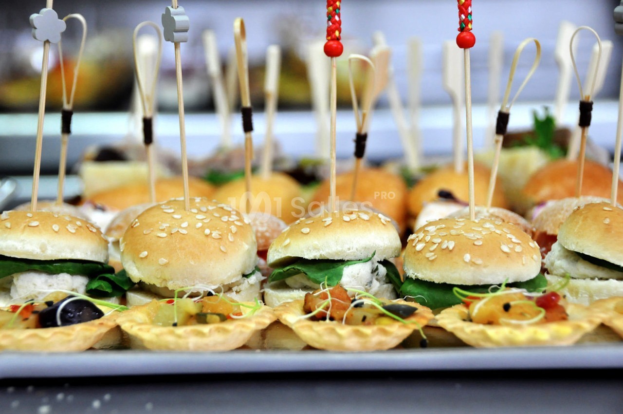 Plateau de mini-burgers garnis de salade et de bouchées apéritives décorées de piques en bois.