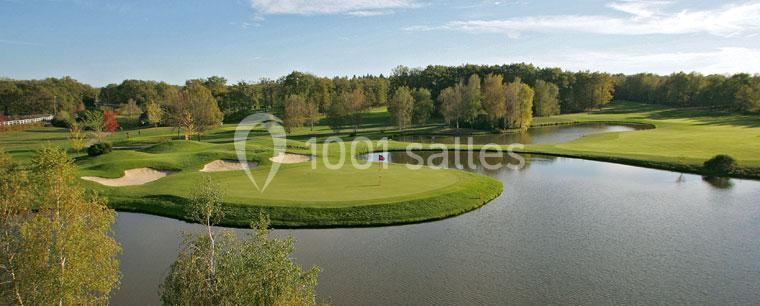 Vue d'un parcours de golf avec un green entouré d'eau, des bunkers et des arbres en arrière-plan.