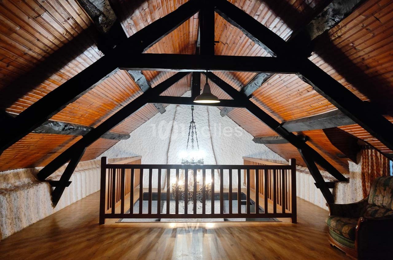 Plafond en bois avec poutres apparentes, balustrade en bois et lumière suspendue dans un espace mansardé.