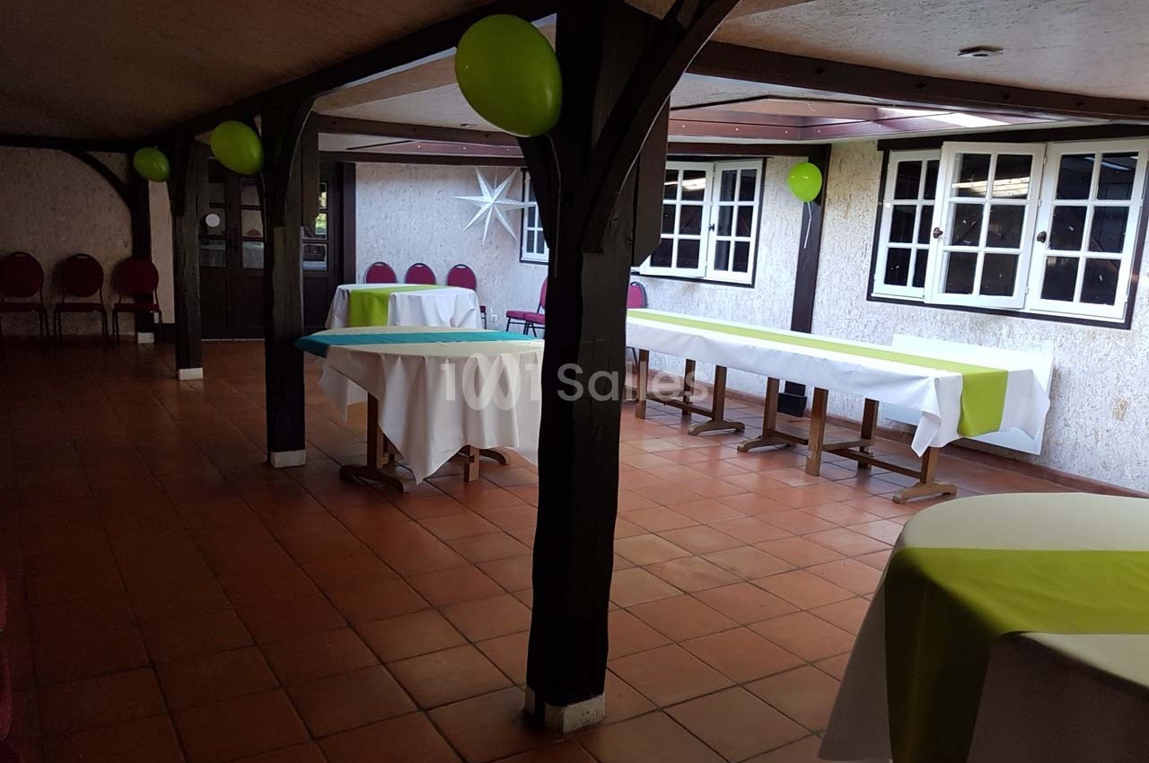 Salle décorée avec des ballons verts, tables recouvertes de nappes blanches et vertes, sol en carrelage.