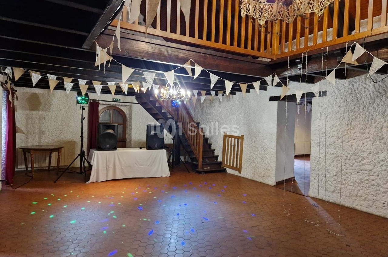 Salle de réception avec poutres apparentes, guirlandes de fanions, éclairage coloré et espace de danse.