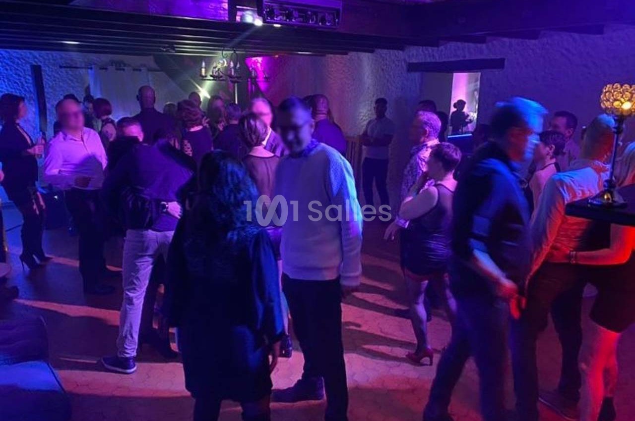 Des personnes dansent et discutent dans une salle éclairée par des lumières violettes et tamisées.