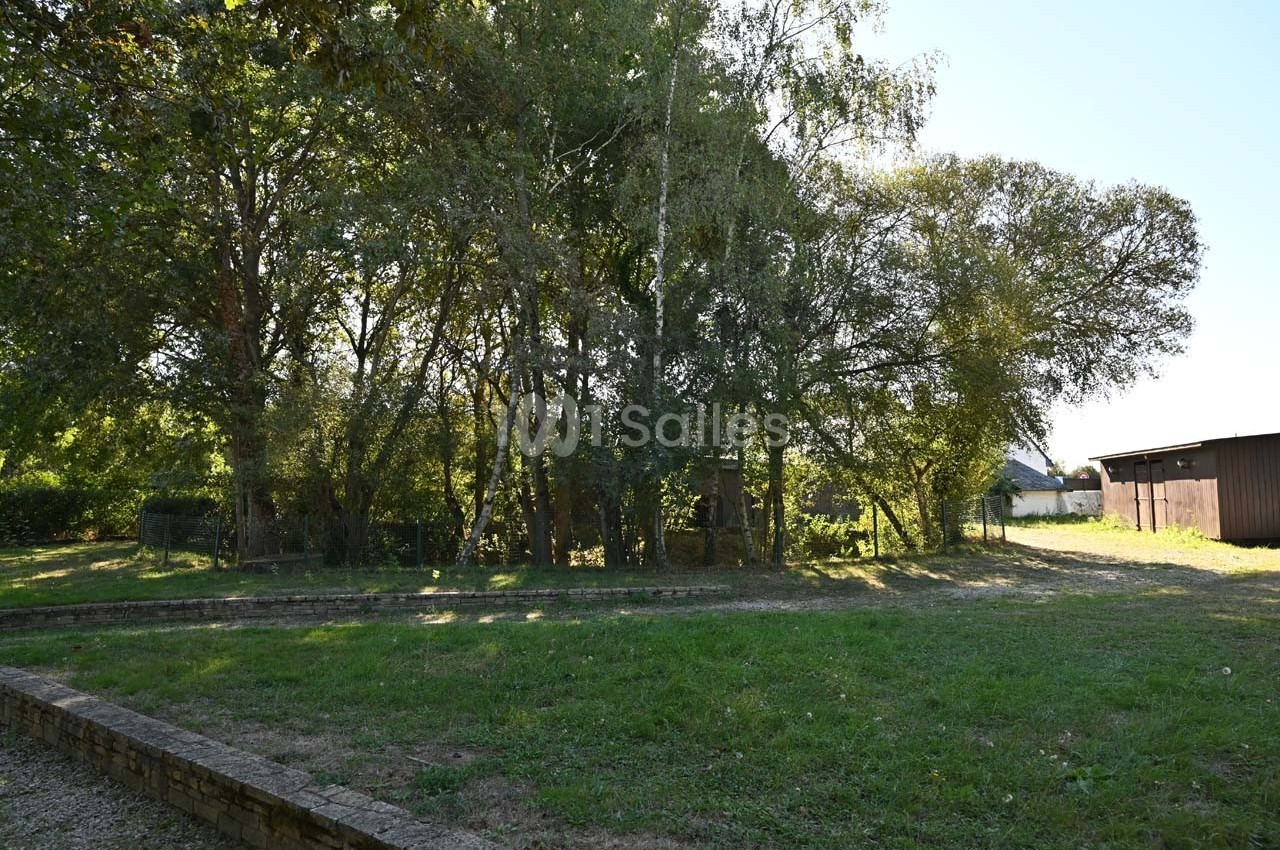 Un espace herbeux bordé d'arbres avec une cabane en bois visible à travers le feuillage.