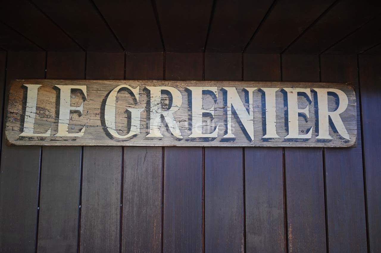 Panneau en bois vieilli avec l'inscription ’Le Grenier’ fixé sur un mur en bois sombre.