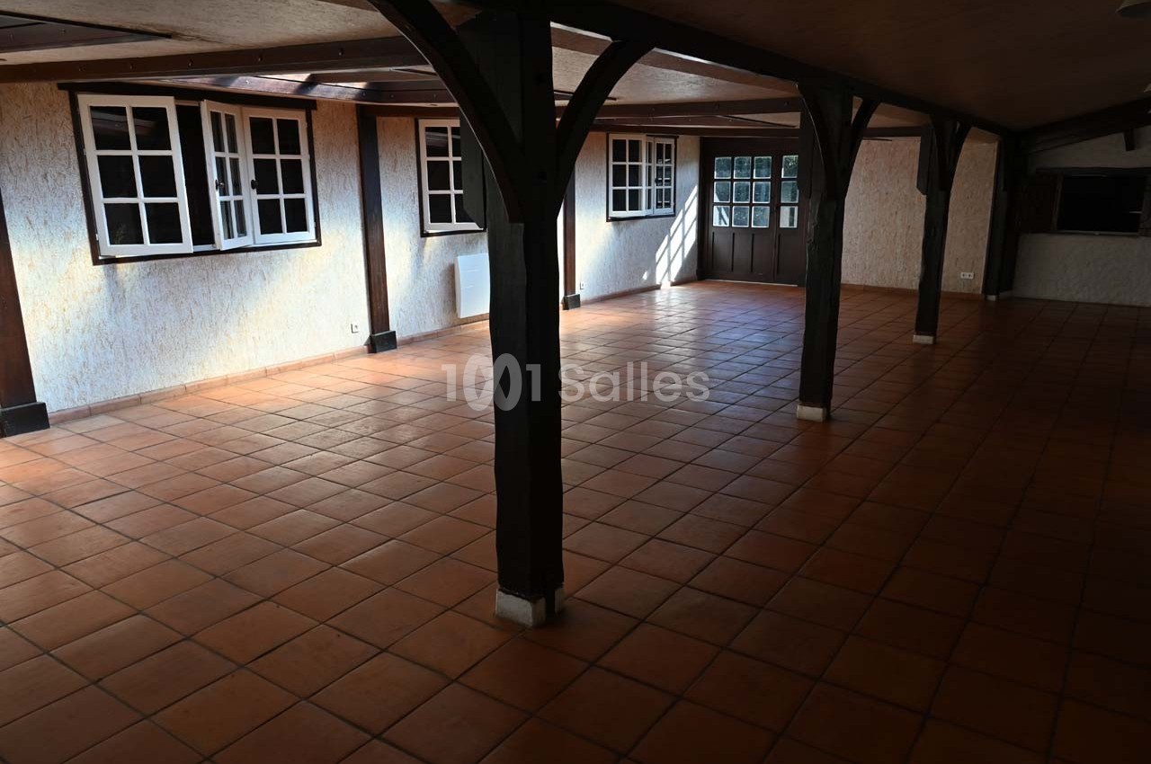 Salle spacieuse avec carrelage en terre cuite, poutres en bois et plusieurs fenêtres laissant entrer la lumière naturelle.