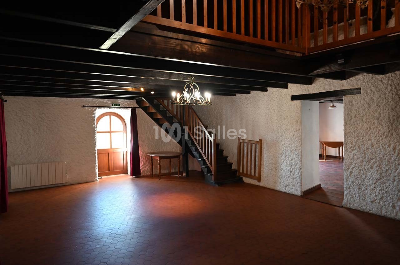 Salle intérieure avec murs en pierre blanche, escalier en bois, lustre suspendu et lumière naturelle provenant d'une porte…