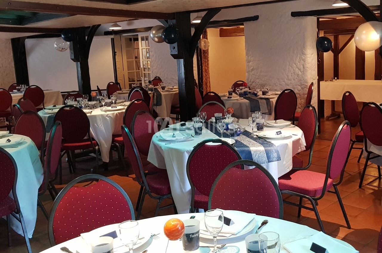 Salle de réception décorée avec des tables rondes dressées, nappes blanches et chaises rouges.