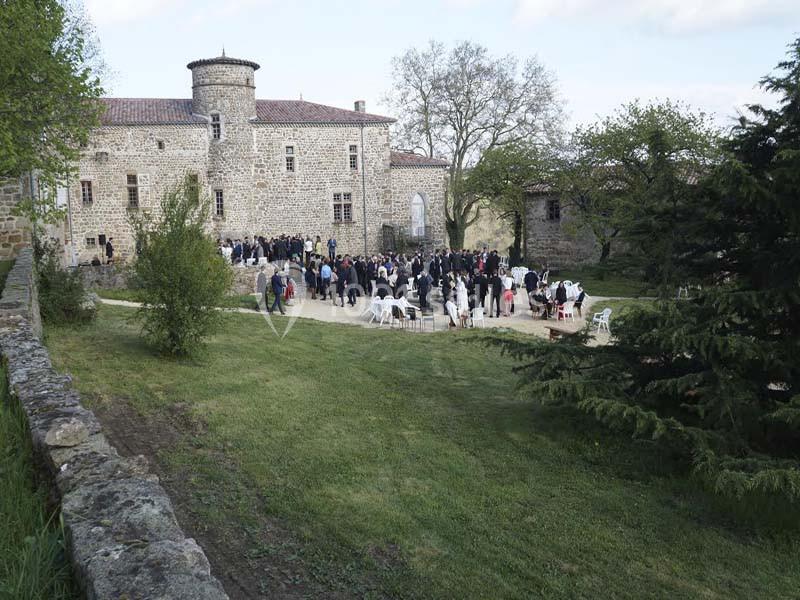 Groupe de personnes rassemblées dans la cour d'un château en pierre entouré de verdure.