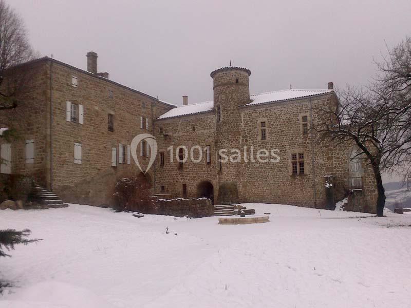 Château en pierre entouré de neige, avec une tour centrale et des arbres dénudés en arrière-plan.