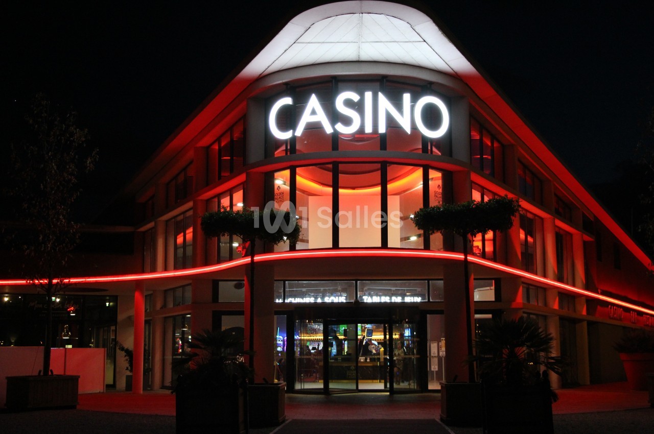 Façade d'un casino éclairée par des néons rouges et blancs, avec des plantes en premier plan, de nuit.