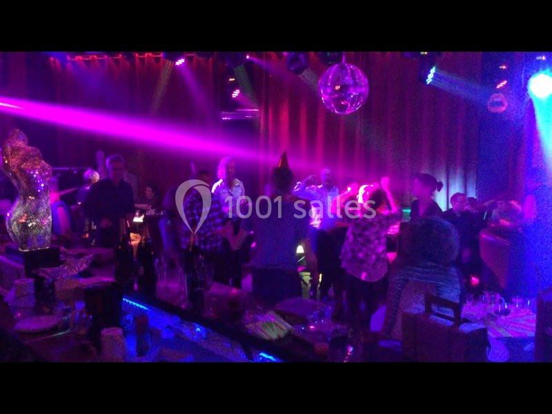 Des personnes dansent sous des lumières colorées dans une ambiance festive, entourées de tables et de décorations.
