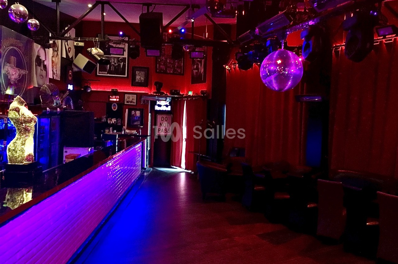 Intérieur d'un bar ou d'une discothèque avec éclairage tamisé, comptoir lumineux et boule disco suspendue.