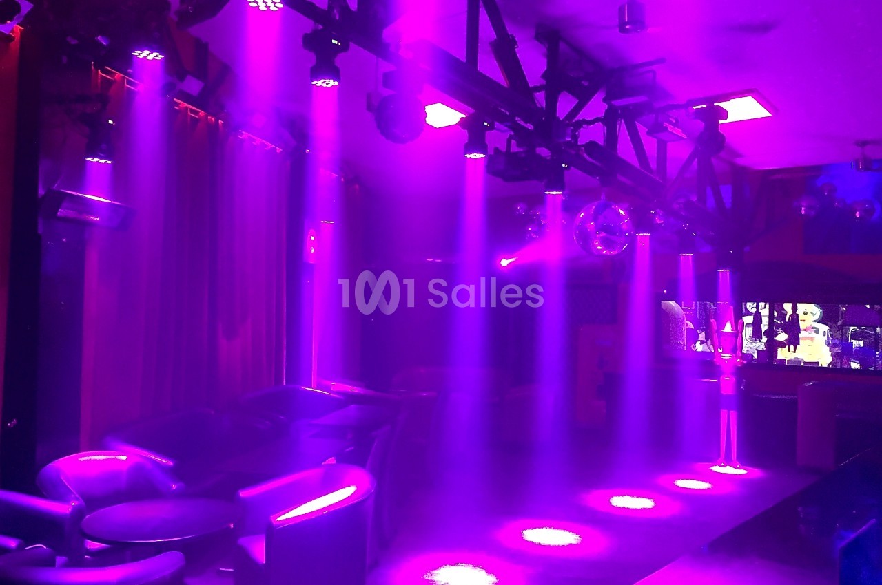 Salle sombre avec des fauteuils, éclairée par des projecteurs violets et une boule disco suspendue.
