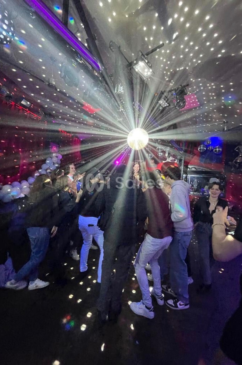 Des personnes dansent sous une boule à facettes dans une salle éclairée par des lumières colorées et des spots.