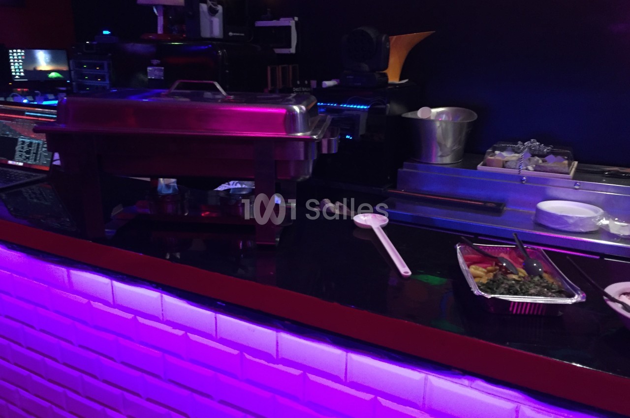 Buffet chaud en acier inoxydable sur un comptoir éclairé par des lumières violettes, avec des plats en préparation.