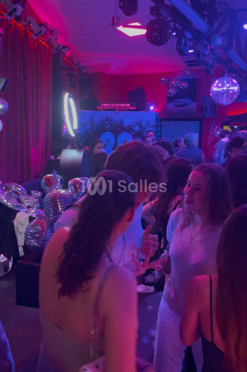 Des personnes discutent et dansent dans une ambiance festive avec éclairage coloré et boules à facettes.
