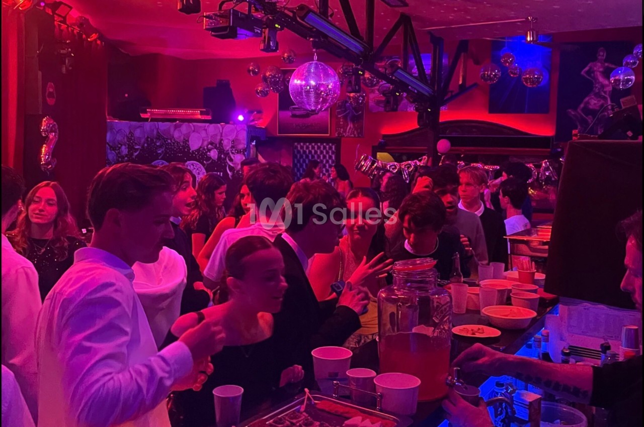 Des jeunes discutent et se servent à un buffet dans une ambiance festive avec éclairage coloré et décorations.