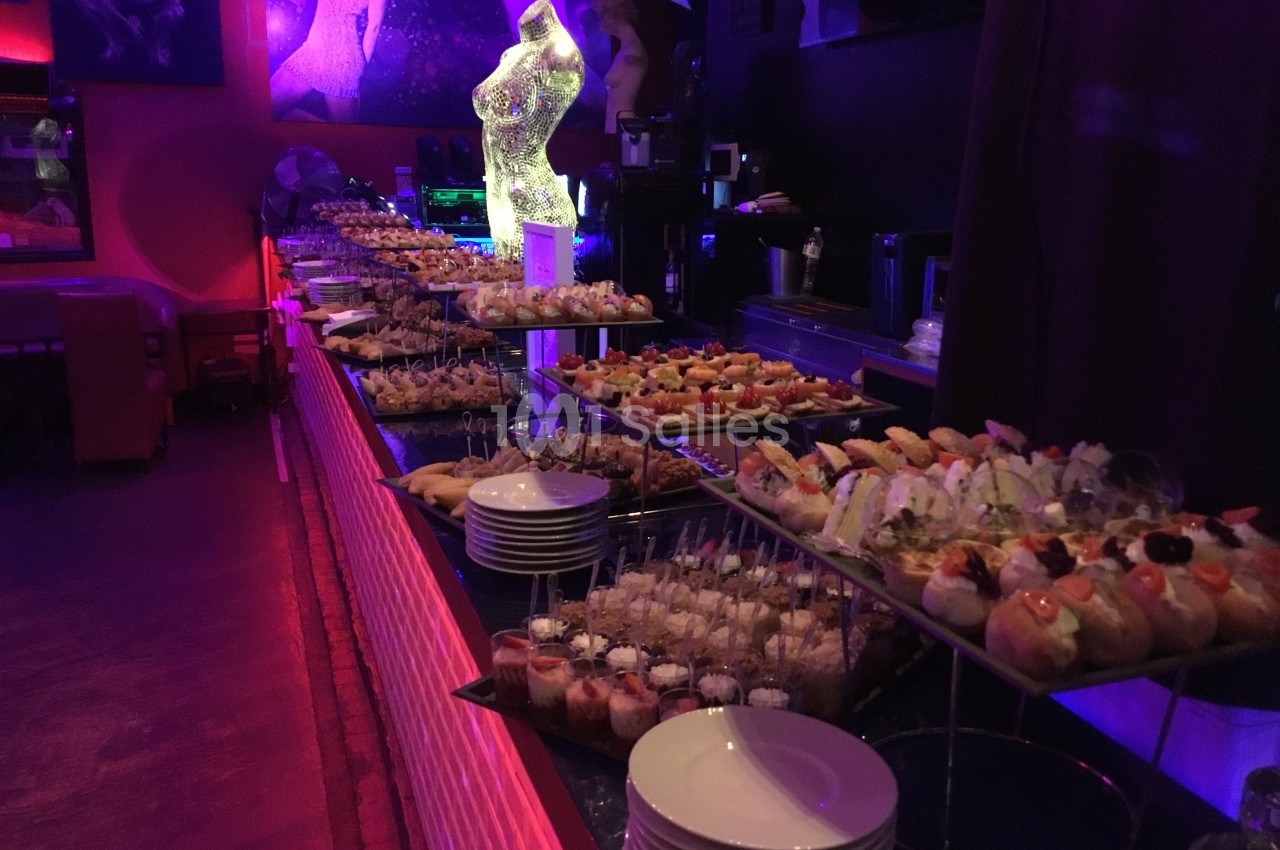 Buffet de cocktails et amuse-bouches variés disposés sur des étagères dans une salle à l'éclairage tamisé.