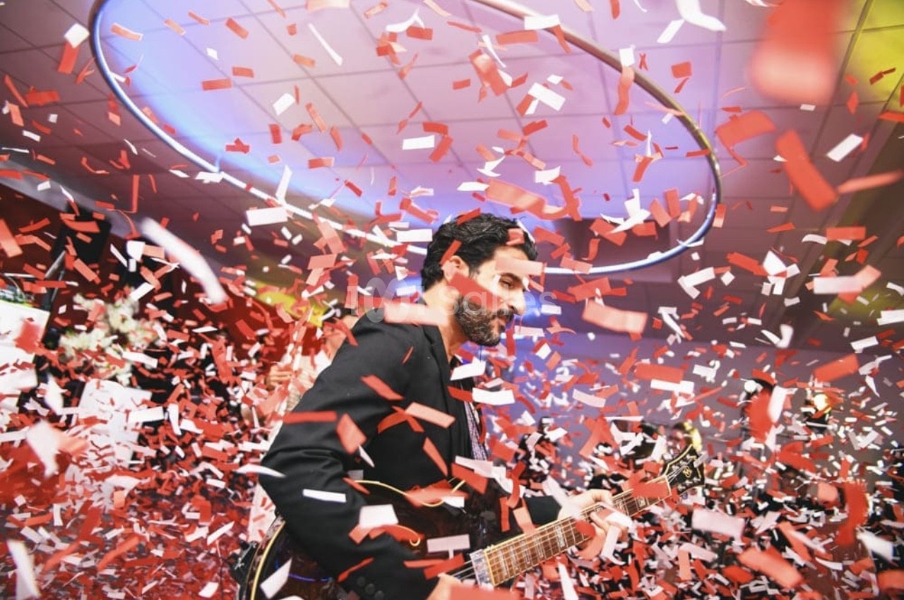 Un musicien jouant de la guitare entouré de confettis rouges et blancs dans un lieu festif.