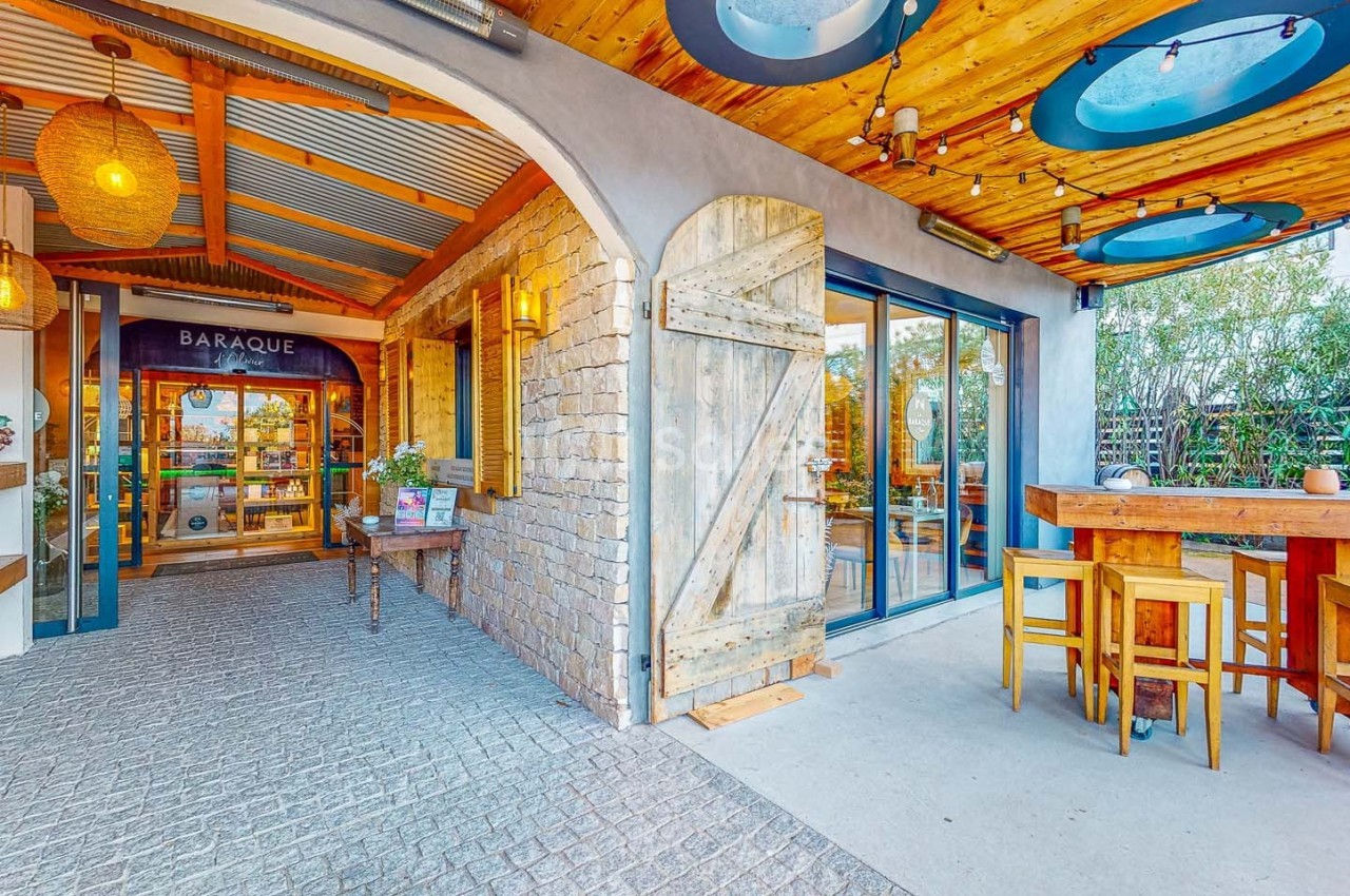Entrée d'un restaurant avec porte en bois, terrasse couverte, tables hautes et décoration chaleureuse.