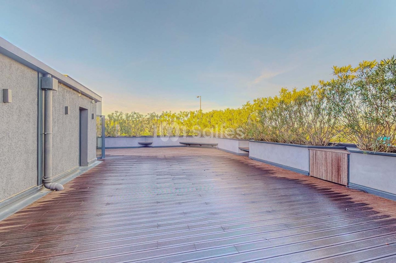 Terrasse en bois spacieuse avec balustrades blanches, entourée de végétation sous un ciel dégagé.