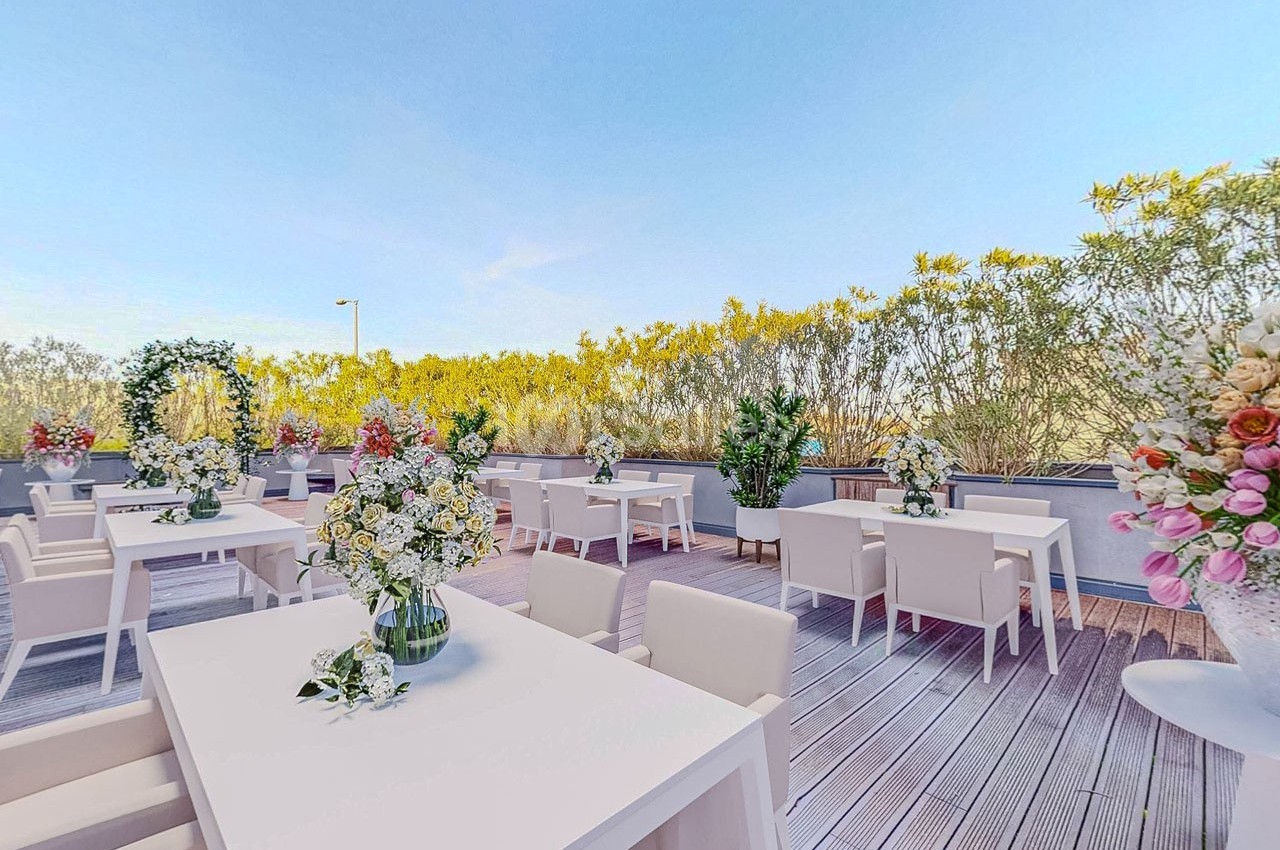 Terrasse aménagée avec des tables blanches, des chaises et des compositions florales, entourée de végétation.