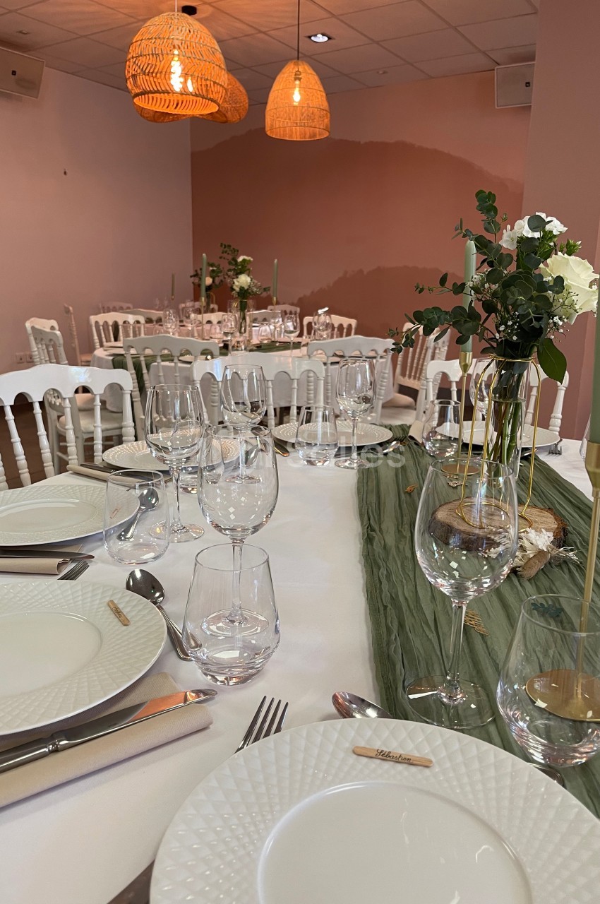 Table dressée avec vaisselle blanche, verres et bougies, décorée de fleurs et d'un chemin de table vert dans une salle…