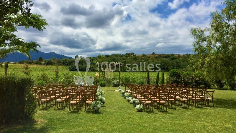 Chaises disposées en rangées sur une pelouse face à une arche décorée, dans un cadre champêtre avec des montagnes en arrière…