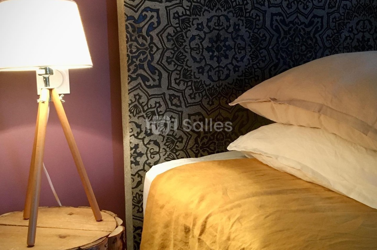 Lit avec une tête de lit à motifs géométriques, draps jaunes, lampe sur trépied et table de chevet en bois.