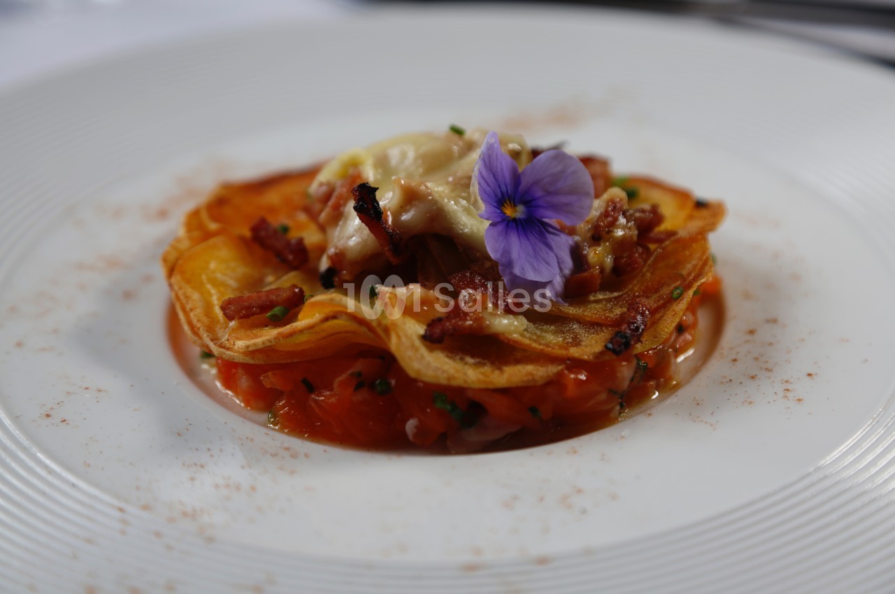 Assiette garnie d'une fine galette croustillante, saumon, lardons et fleur comestible en décoration.
