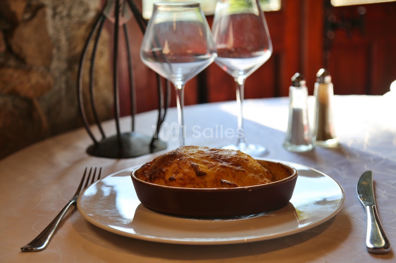 Plat gratiné dans un ramequin en céramique, servi sur une table dressée avec couverts, verres et condiments.