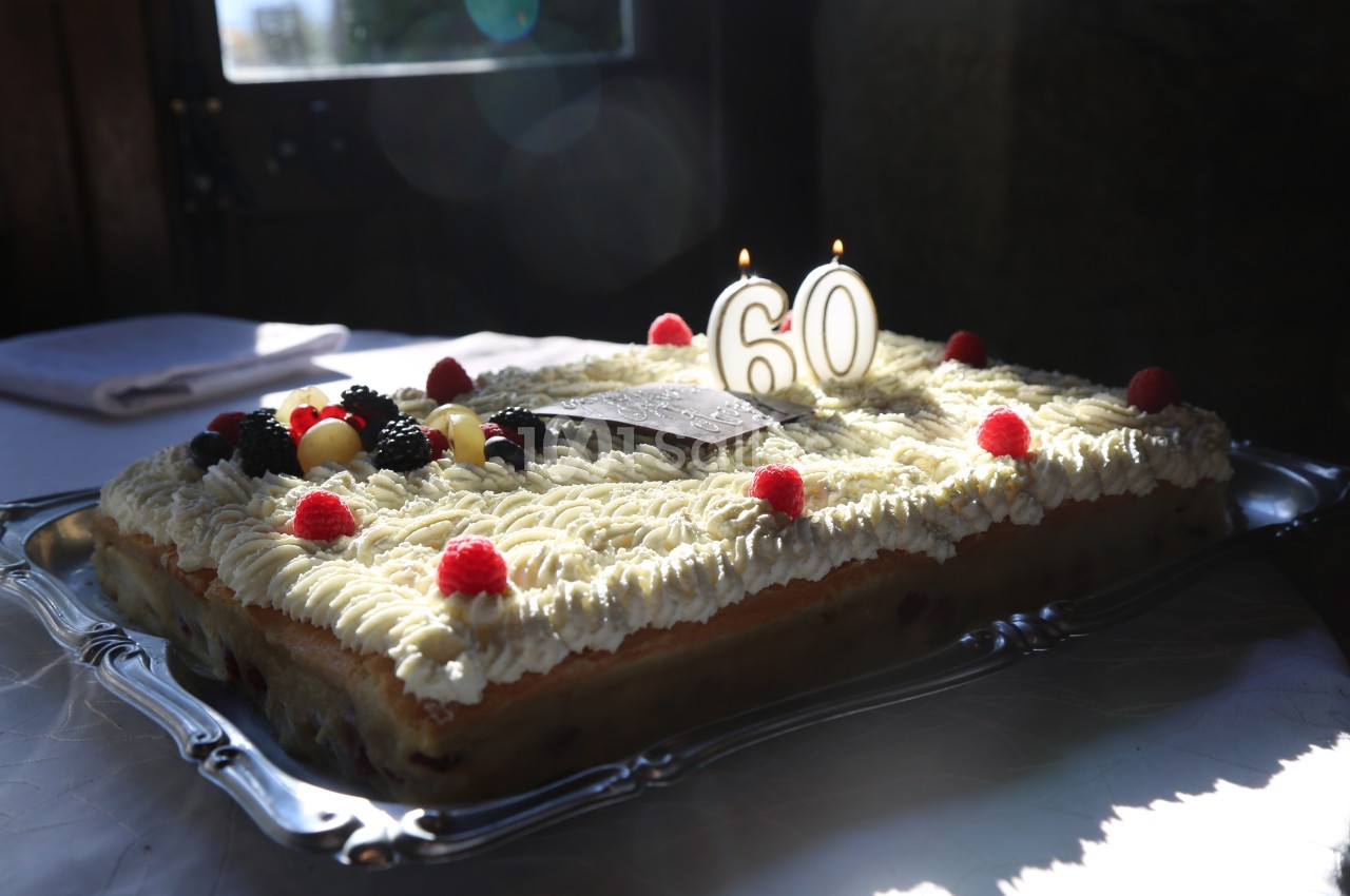 Gâteau rectangulaire décoré de fruits rouges, de crème et de bougies indiquant le chiffre 60, posé sur un plateau argenté.