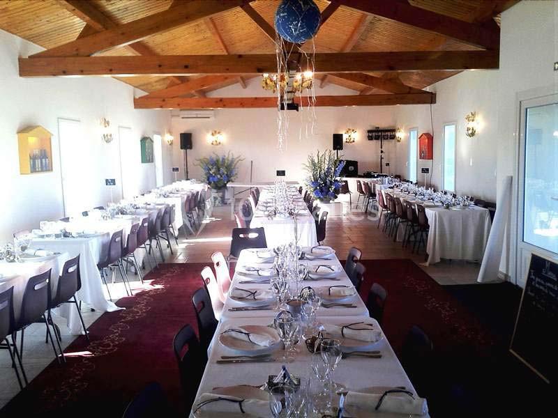 Salle de réception décorée avec des tables dressées pour un événement, éclairée par la lumière naturelle.