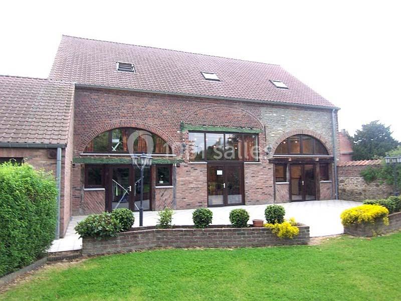 Façade en briques d'un bâtiment avec grandes fenêtres cintrées, terrasse pavée et jardin entretenu au premier plan.