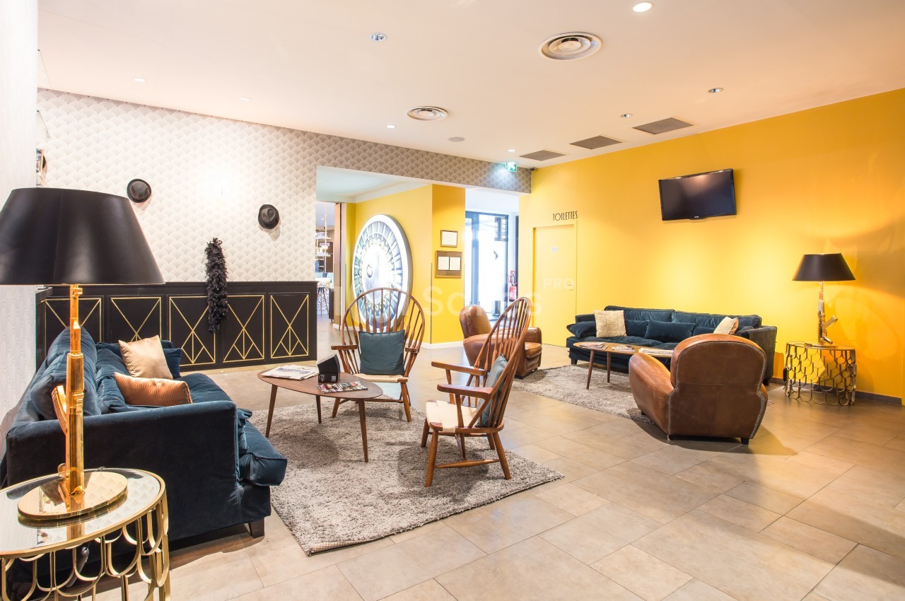 Salon lumineux avec murs jaunes, mobilier vintage, canapés en velours, fauteuils en bois et décoration élégante.
