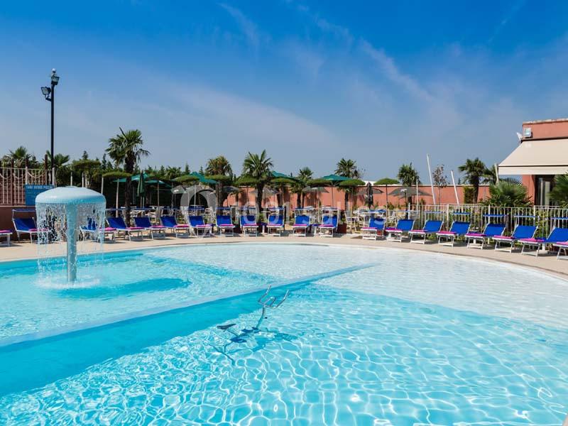 Piscine extérieure avec fontaine, entourée de transats bleus et de parasols, sous un ciel dégagé.