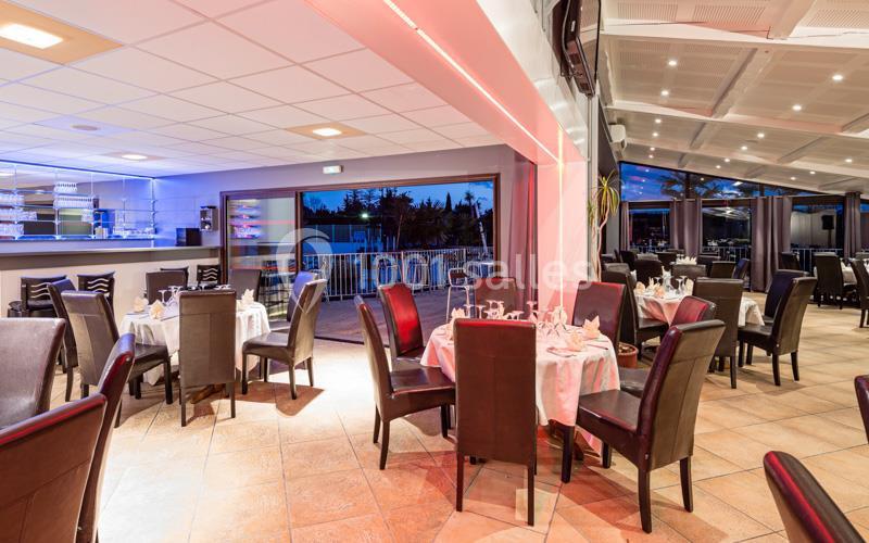 Salle de restaurant lumineuse avec tables dressées, chaises en cuir sombre et vue sur une terrasse extérieure.